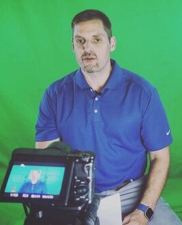 Young man in early 40's with blue polo shirt with a green screen behind him