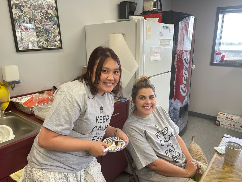Nika and Taylar sitting in the Northwest Custom Apparel lunchroom celebrating their June birthday with cake in hands